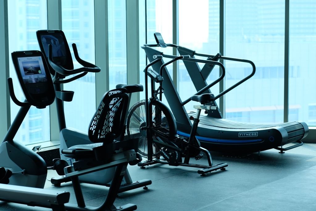 Sudut kardio Sinergi Fit dengan sepeda statis, air bike, dan curved treadmill di depan jendela