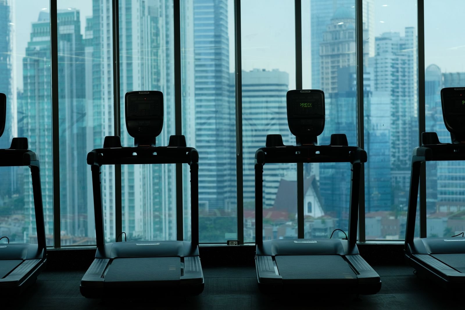 Deretan treadmill Sinergi Fit menghadap jendela dengan pemandangan gedung-gedung Jakarta